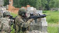 Zwei Soldaten knien hinter einen Mauerrest einer Hausruine und zielen mit ihren Waffen ins Gelände.
