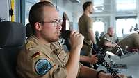 Ein Soldat mit Brille hält ein Funkgerät in seiner rechten Hand