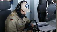 Ein Soldat mit Headset auf dem Kopf schreibt in ein Buch 