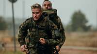 Soldatin mit Rucksack joggt vor einem Soldaten