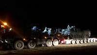 Im Scheinwerferlicht fährt ein Panzer auf einen Schwerlasttransporter. 