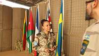 Eine Frau in Uniform steht einem Mann in schwedischer Uniform gegenüber. Sie unterhalten sich. Im Hintergrund hängen Flaggen.