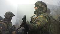 Ein Soldat mit Gewehr im Nebel auf einer Wiese schreit, daneben stehen weitere Soldaten.