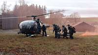 Soldaten tragen eine simulierte verletzte Person in einem Rettungstuch zu einem wartenden Hubschrauber.