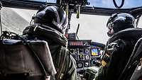Zwei Piloten im Cockpit eines Hubschraubers über See.