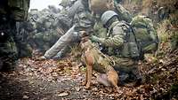 Ein deutscher Soldat hockt neben einem Hund im Gelände während einer Übung.