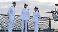 Zwei Soldaten und eine Soldatin stehen mit weißen Uniformen auf dem Deck eines Schiffs