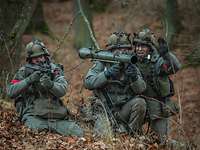 Drei Soldaten kniend im Wald mit Waffen im Anschlag