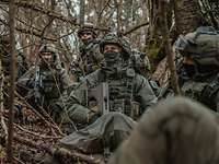 Fünf Soldaten kniend im Wald mit Waffen in der Hand