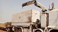 Ein weißer LKW im Wünstensand mit einem ausgefahrenen Lastenkran und Anhänger
