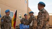 Ein Soldat steht in formaler Haltung vor einem Gebäude. Drei weitere Soldaten stehen vor und neben ihm.