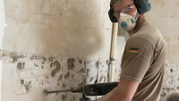 Hauptmann Adrian Baral entfernt mit einem Bohrhammer den Putz von einer Hauswand