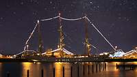 Eine weißes beleuchtetes Segelschiff bei Nacht.