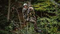 Ein Soldat und ein Hund hängen zusammen an einer Seilrutsche im Wald.