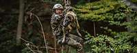 Ein Soldat und ein Hund hängen zusammen an einer Seilrutsche im Wald.