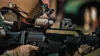 Ein Soldat blickt durch ein Zielfernrohr und schießt draußen mit seinem Gewehr. 