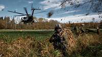 Mehrere Soldaten knien an einer Waldlichtung, dahinter landet ein Hubschrauber.