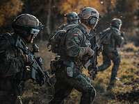 Vier Soldaten stürmen im Abendrot nebeneinander über eine Waldlichtung.