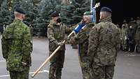 Zwei Soldaten stehen sich auf einem Appellplatz gegenüber und halten eine blaue Truppenfahne. 