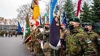 Mehrere Soldaten stehen mit bunten Truppenfahnen auf einem Appellplatz nebeneinander.