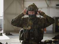 Ein Soldat mit Trageausrüstung setzt sich in einer Halle einen Helm mit Gehörschutz auf. Sein Blick ist konzentriert.