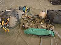 Die Ausrüstung eines Soldaten liegt ausgebreitet auf einer grünen Plane in einer Halle.