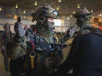 Ein Soldat mit Helm und Tuch im Gesicht steht mit hochgehaltenen Händen vor einem Soldaten, der die Ausrüstung kontrolliert.