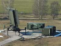 RAT 31 DL/M in der Stellung Schönewalde Zwei olivgrüne Container stehen auf einer kreisförmigen Betonplatte. Vor ihnen ist ein senkrecht stehendes Radar aufgebaut