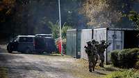 Drei Soldaten mit Waffen im Anschlag stürmen zwischen Containern.