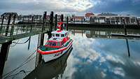 Ein Motorboot mit weiß und leuchtend rot gestrichenen Aufbauten liegt in einem kleinen Hafen.