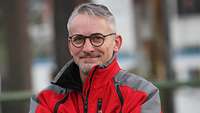 Porträtbild eines Mannes mit Brille in roter Jacke.