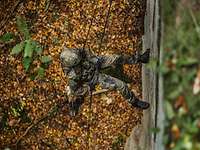 Blick auf einen Soldaten, der sich mit einem Hund auf dem Rücken von einer Felswand abseilt.