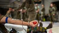 Ein Soldat liegt auf einer Liege und bekommt Blut abgenommen. Er hält einen kleinen roten Ball in der Hand.