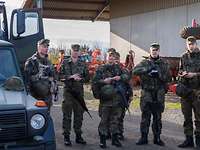 Zur Befehlsausgabe stehen die Soldaten vor einer Scheune und Landwirtschaftsgeräten.