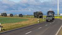 Verschiedene Militärfahrzeuge Logistikbataillons 467 fahren in Kolonne auf einer zivilen Straße.