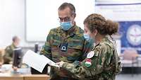 A hungarian soldier and a Belgian soldier discuss a manuscript