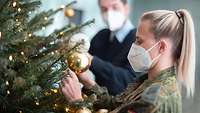 Eine Soldatin und ein Soldat schmücken einen Weihnachtsbaum.