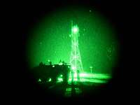Nachtsichtgerät BONIE-M Blick durch ein Nachtsichtgerät vom Typ Bonie-M. In einem grünen Lichtkreis stehen Soldaten neben einem Fahrzeug vor einem Mast.