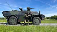 Ein Soldat steht mit Gewehr im Anschlag an der geöffneten Tür eines gepanzerten Radfahrzeuges.