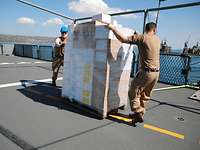 Die Versorger der Fregatte „Schleswig-Holstein“ Zwei Soldaten an einer vollgepackten Palette auf dem Flugdeck eines Schiffes