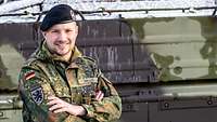Ein Soldat mit schwarzem Barett steht mit verschränkten Armen vor einem Panzer
