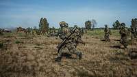 Mehrere bewaffnete Soldaten laufen im Gelände.