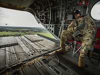 Ein US-amerikanischer Soldat sitzt an der offenen Heckrampe eines Hubschraubers während des Flugs.