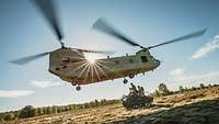 Ein Hubschrauber vom Typ Chinook fliegt dicht über einem Kettenfahrzeug vom Typ Wiesel.