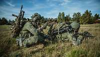 Zwei Soldaten sitzen und liegen mit ihren Waffen im Anschlag im Gelände.