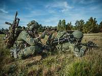 Zwei Soldaten sitzen und liegen mit ihren Waffen im Anschlag im Gelände.