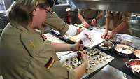 Vorbereiten der Engelsaugen Eine Pfarrerin hat ein Blech mit Plätzchen vor sich liegen und füllt diese mit Marmelade