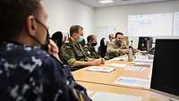 Mehrere Soldaten in Flecktarnuniform sitzen an einem Konferenztisch.