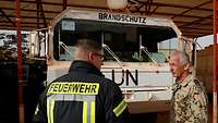 Ein Soldat und ein Feuerwehrmann stehen vor einem weißen LKW.