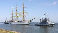 Das Segelschulschiff Gorch Fock im Wasser in Begleitung zweier Boote, die vor und hinter ihm fahren.